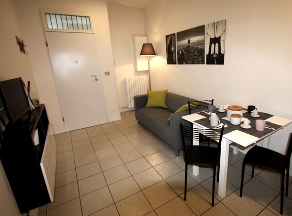 Un petit espace de vie bien aménagé, comprenant un canapé, une table à manger avec des chaises, une lampe et quelques tableaux accrochés au mur.