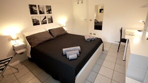 Una camera d'albergo con un letto, comodini, una scrivania, una sedia, uno specchio e una porta.