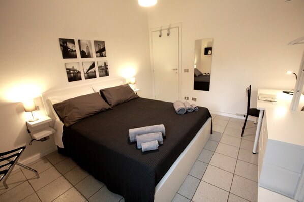 Een hotelkamer met een bed, nachtkastjes, een bureau, een stoel, een spiegel en een deur.