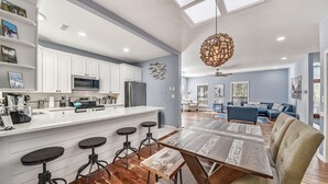 Uma cozinha moderna com armários brancos, uma ilha central com banquetas e uma área de refeições com mesa e cadeiras de madeira.