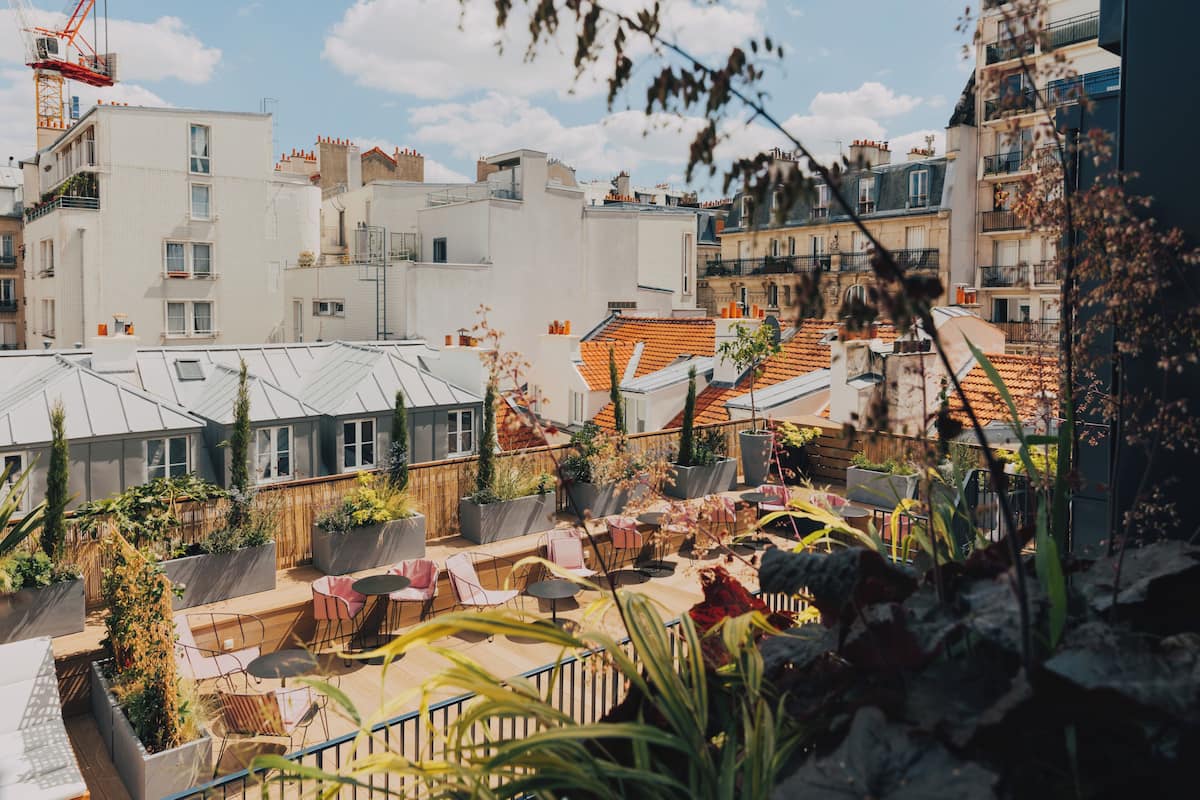 Eine Dachterrasse mit Sitzgelegenheiten und Pflanzen, umgeben von Gebäuden unterschiedlicher Architektur.