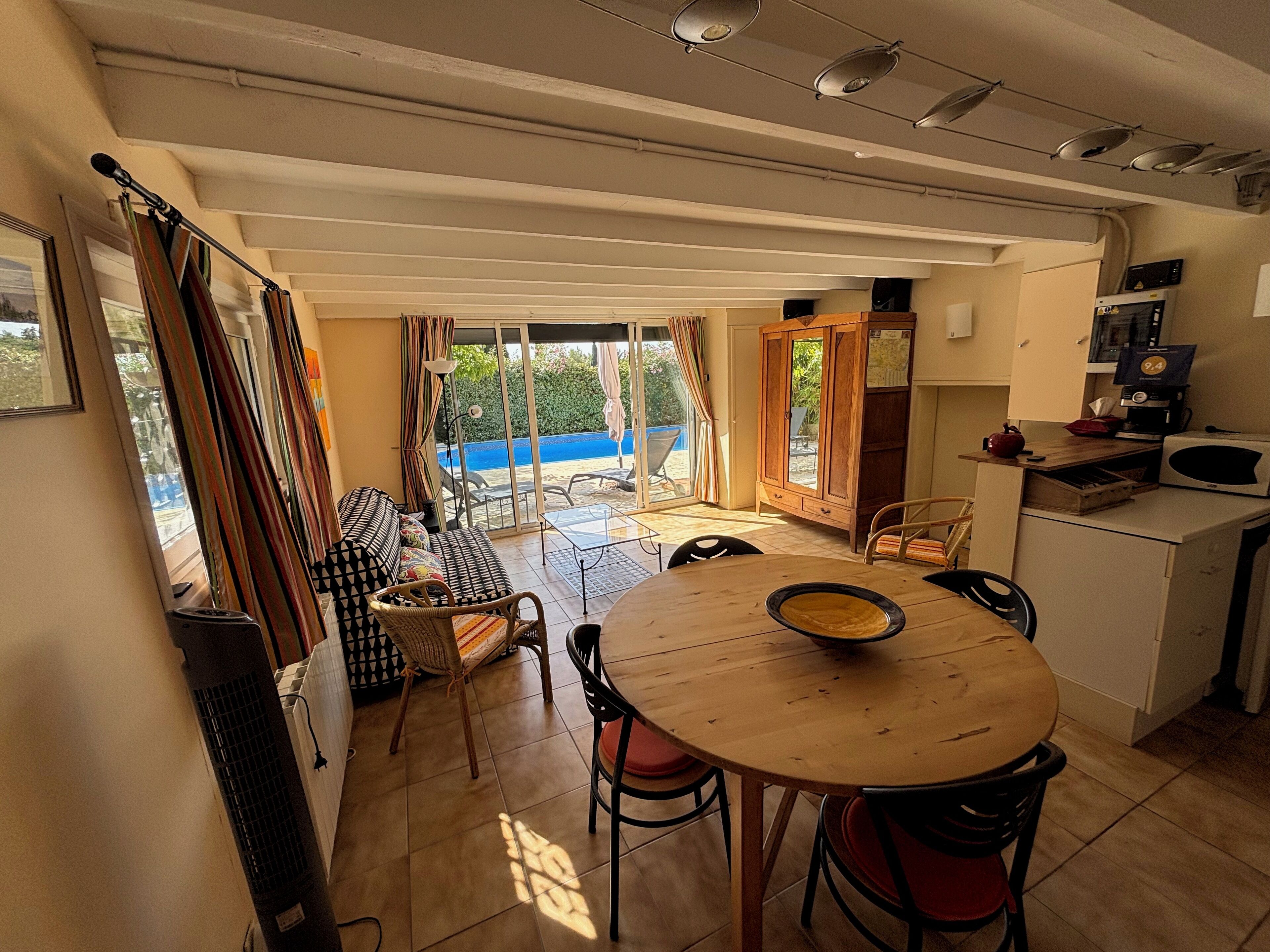 Un coin repas avec une table ronde et des chaises, un coin cuisine équipé d’un four à micro-ondes, et une vue sur un ciel bleu et la verdure, visible à travers la porte vitrée.