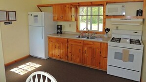 A compact kitchen with wooden cabinets, a refrigerator, a microwave, a stove, and a sink.