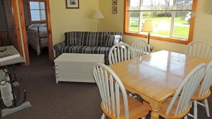 A cozy room with a plaid sofa, a wooden dining table with white chairs, a lamp, and a window with blinds.