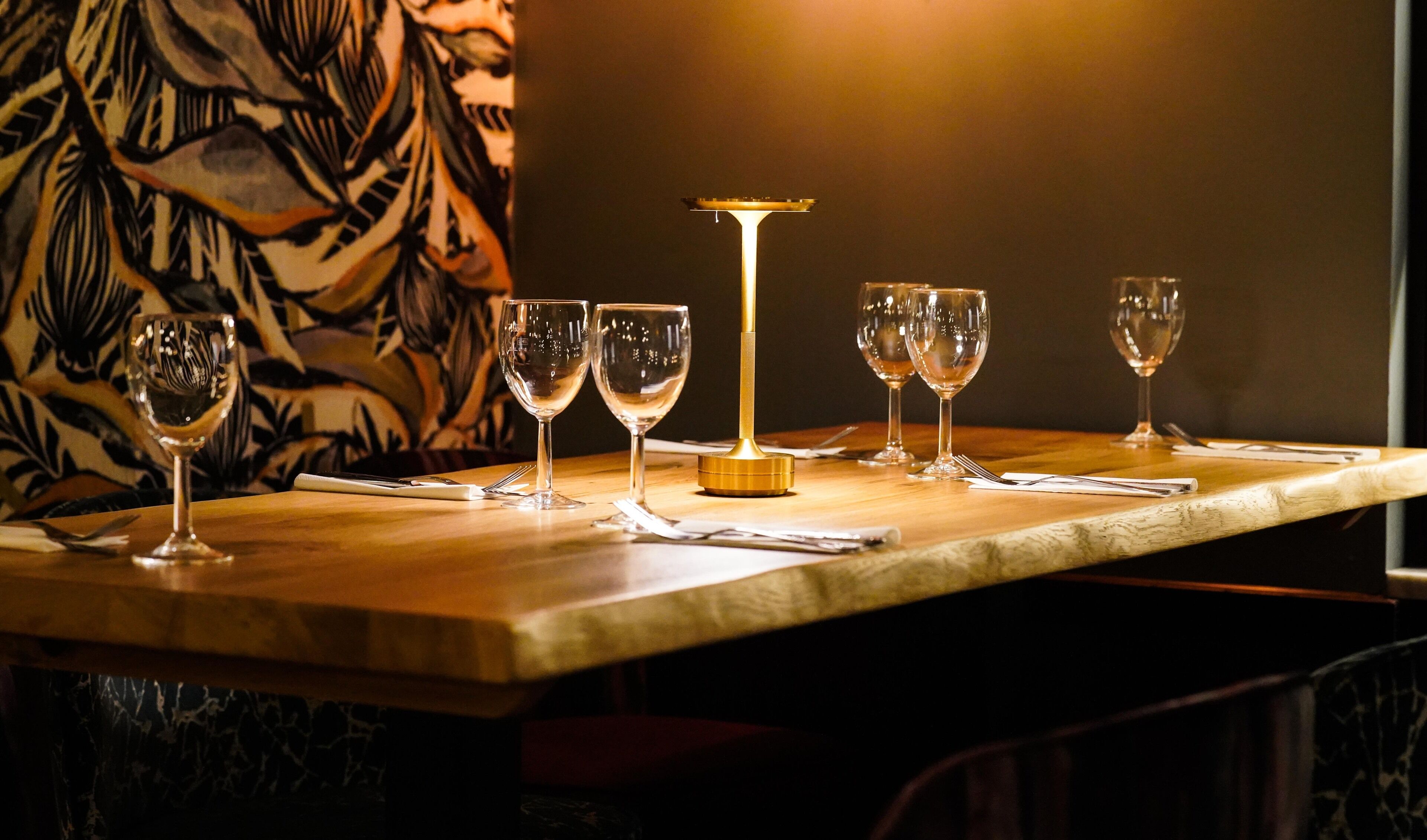A table with six wine glasses and a candle holder, set against a patterned wall.