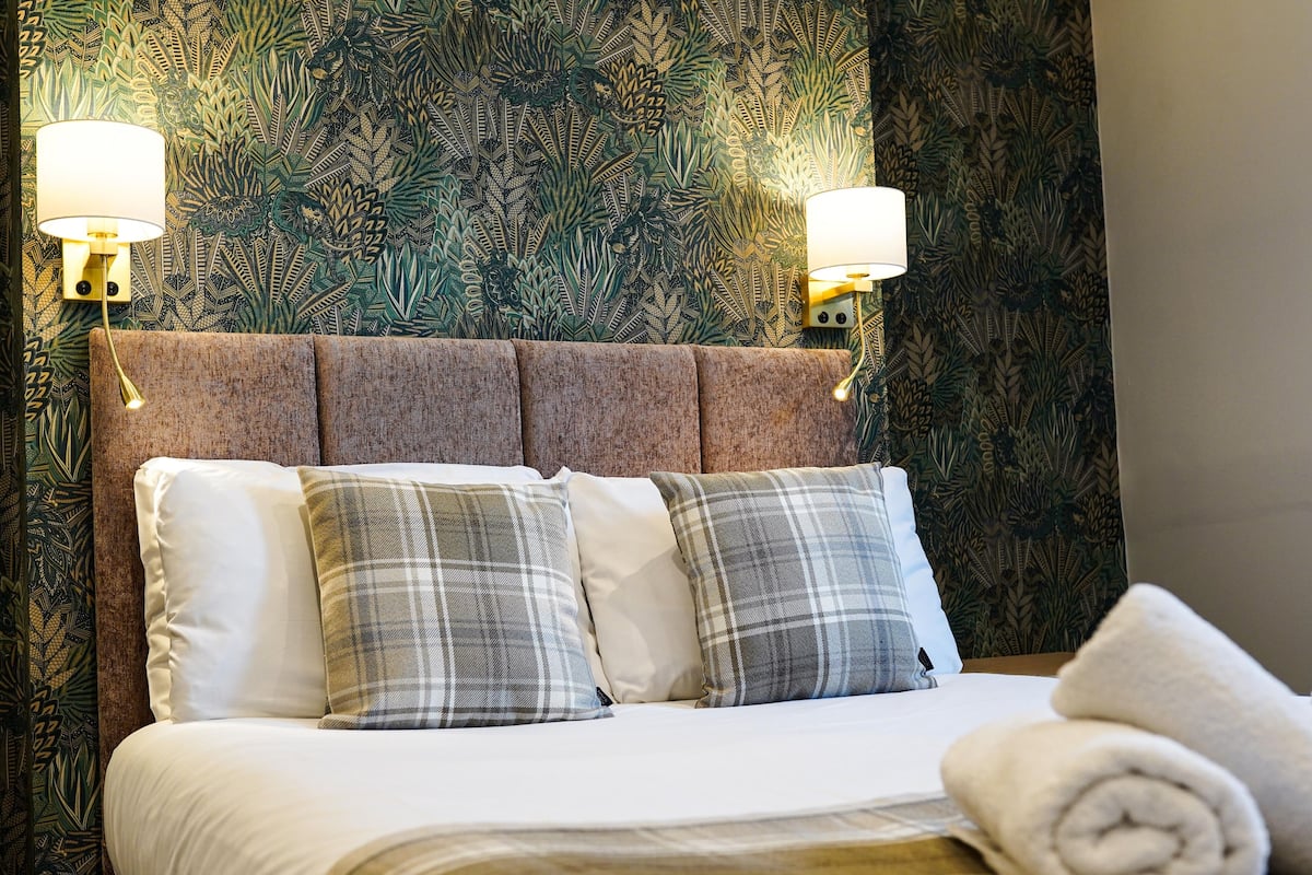 Hotellihuone, jossa on sänky, kaksi seinään kiinnitettyä lamppua ja kuviollinen tapetti.
