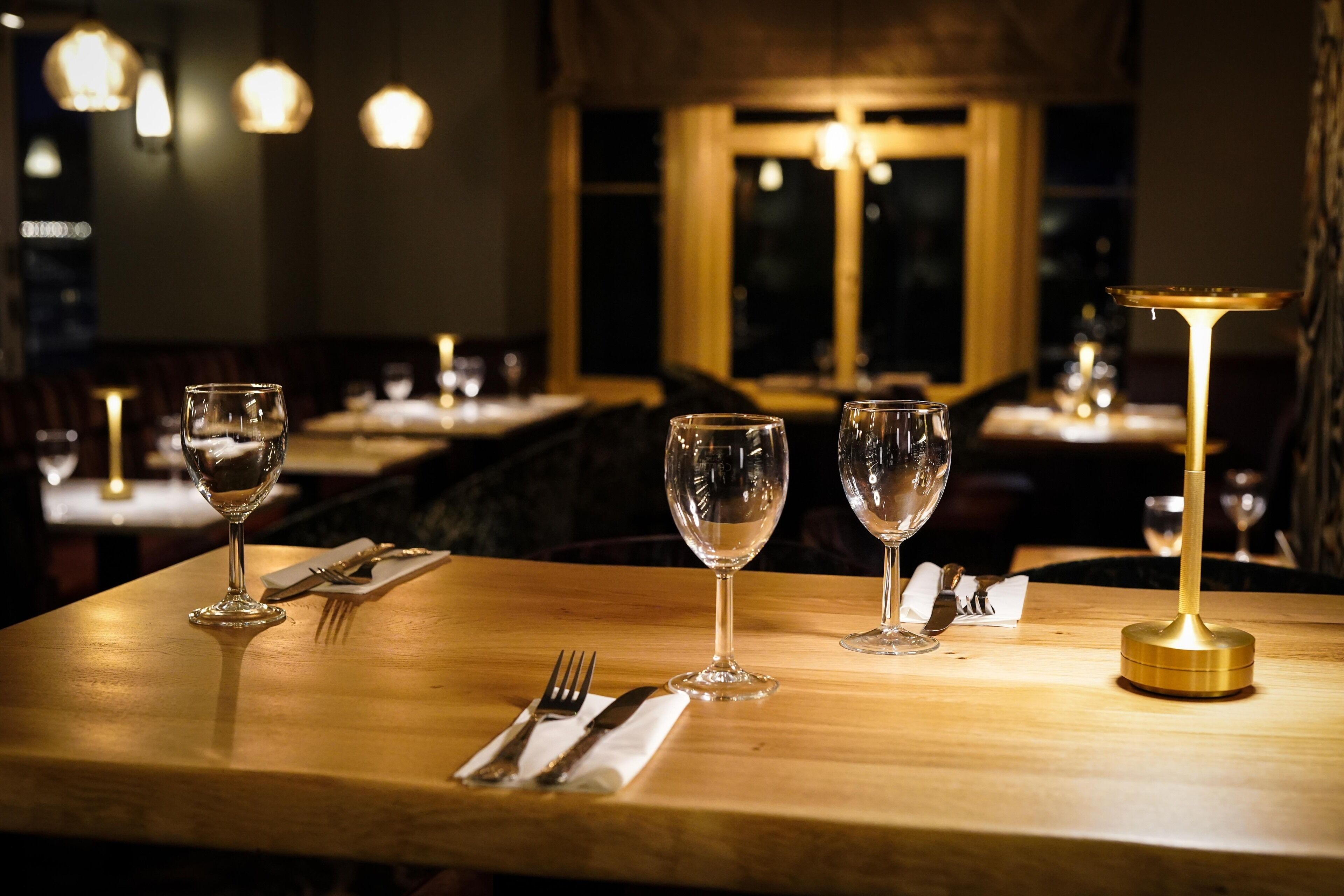 Een restauranttafel met drie wijnglazen, een gouden kandelaar en een bestekset.