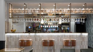Uma área de bar com banquetas, um balcão com garrafas e uma seleção de copos.
