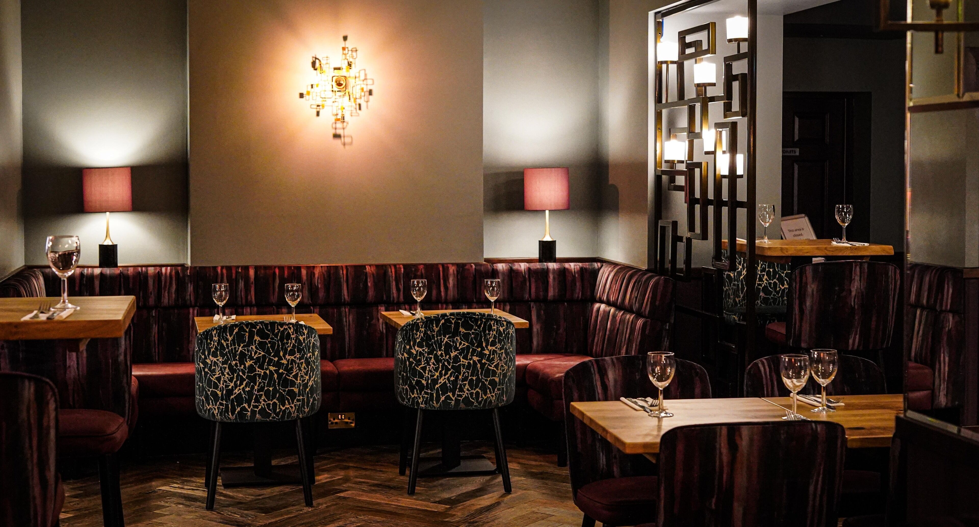 A restaurant interior with leather booths, wooden tables, and a decorative wall light.