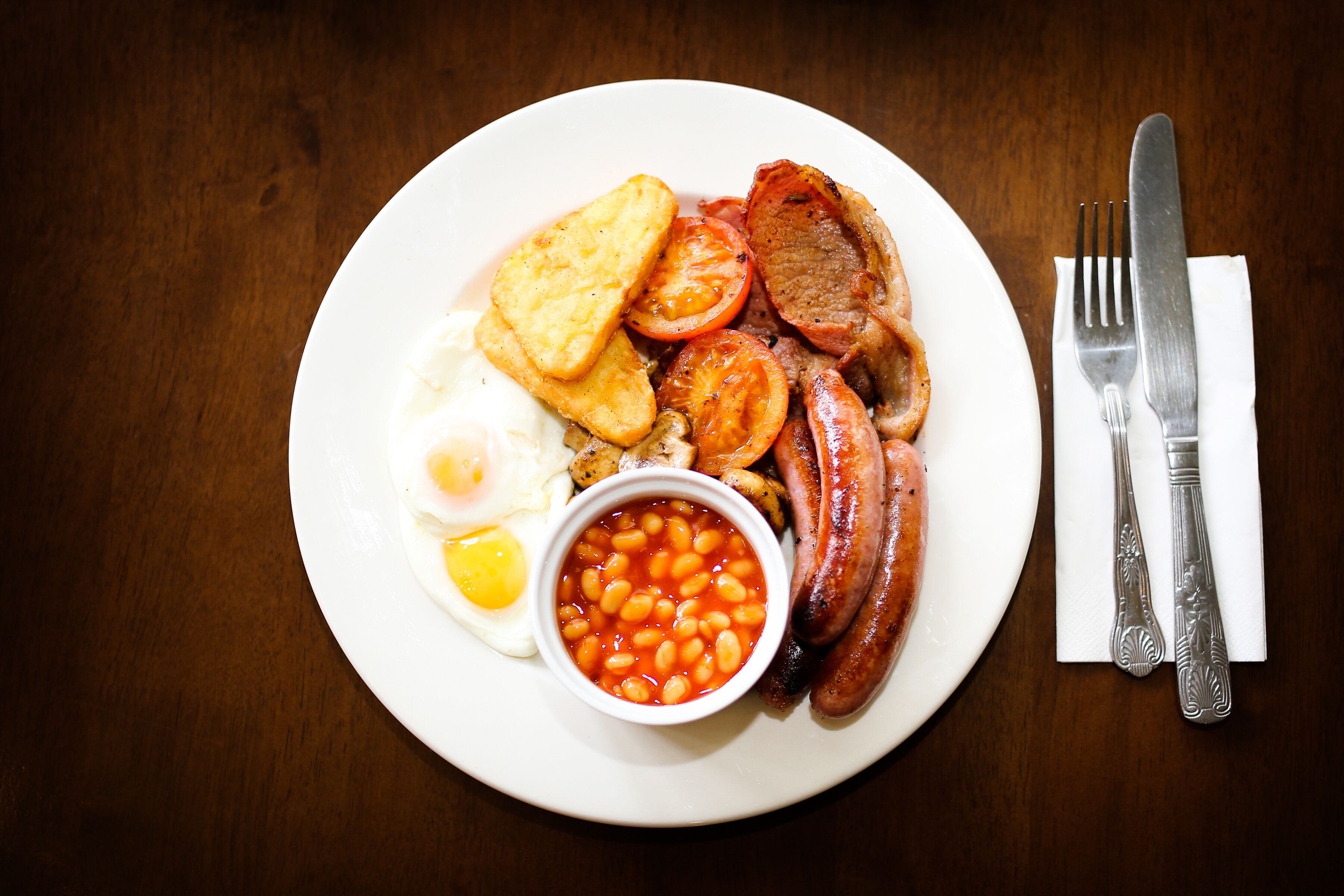 A plate of breakfast food including eggs, sausages, tomatoes, and beans.