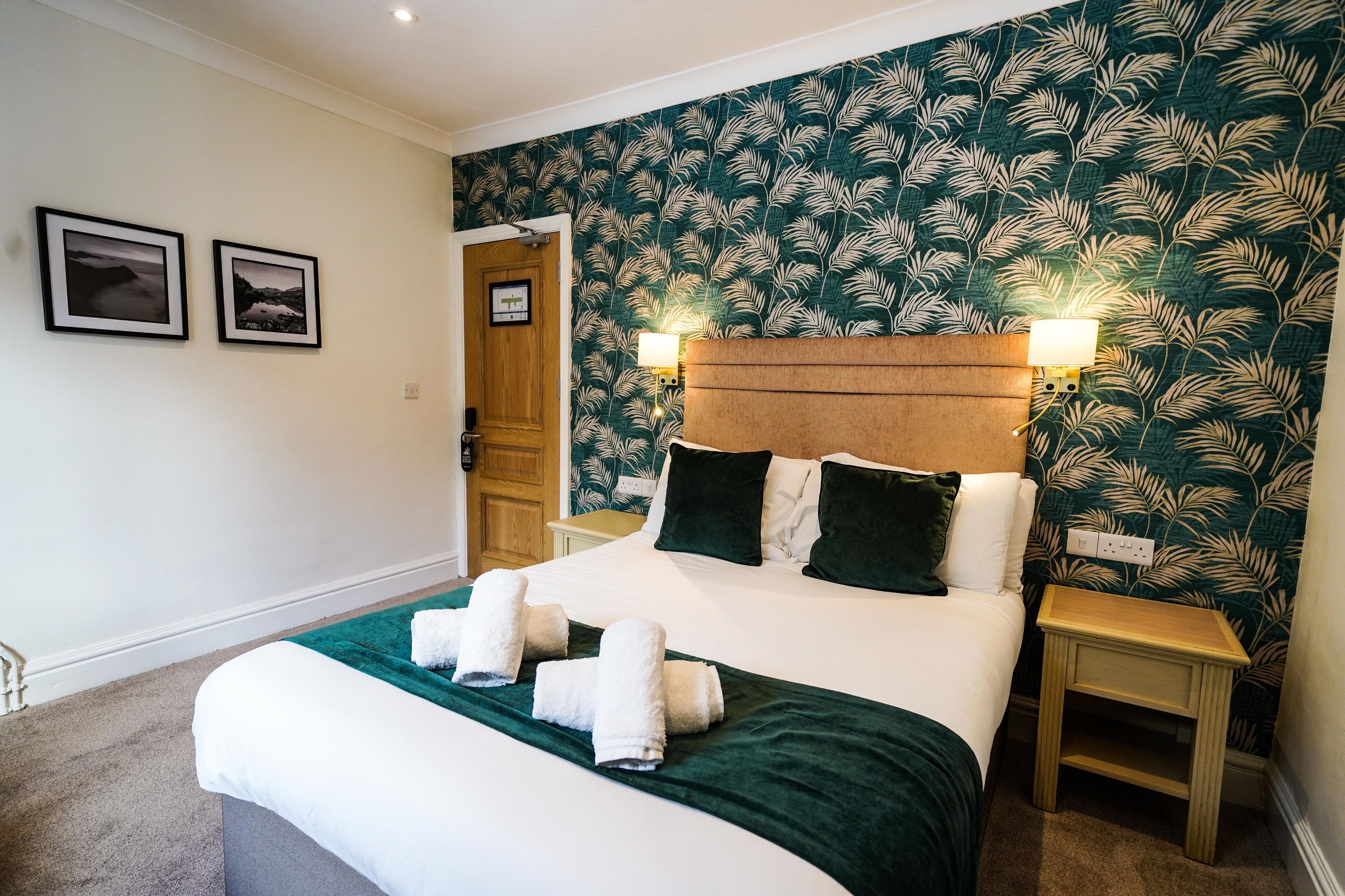 A neatly made bed with white and green bedding, two bedside lamps, and a door leading to another room.