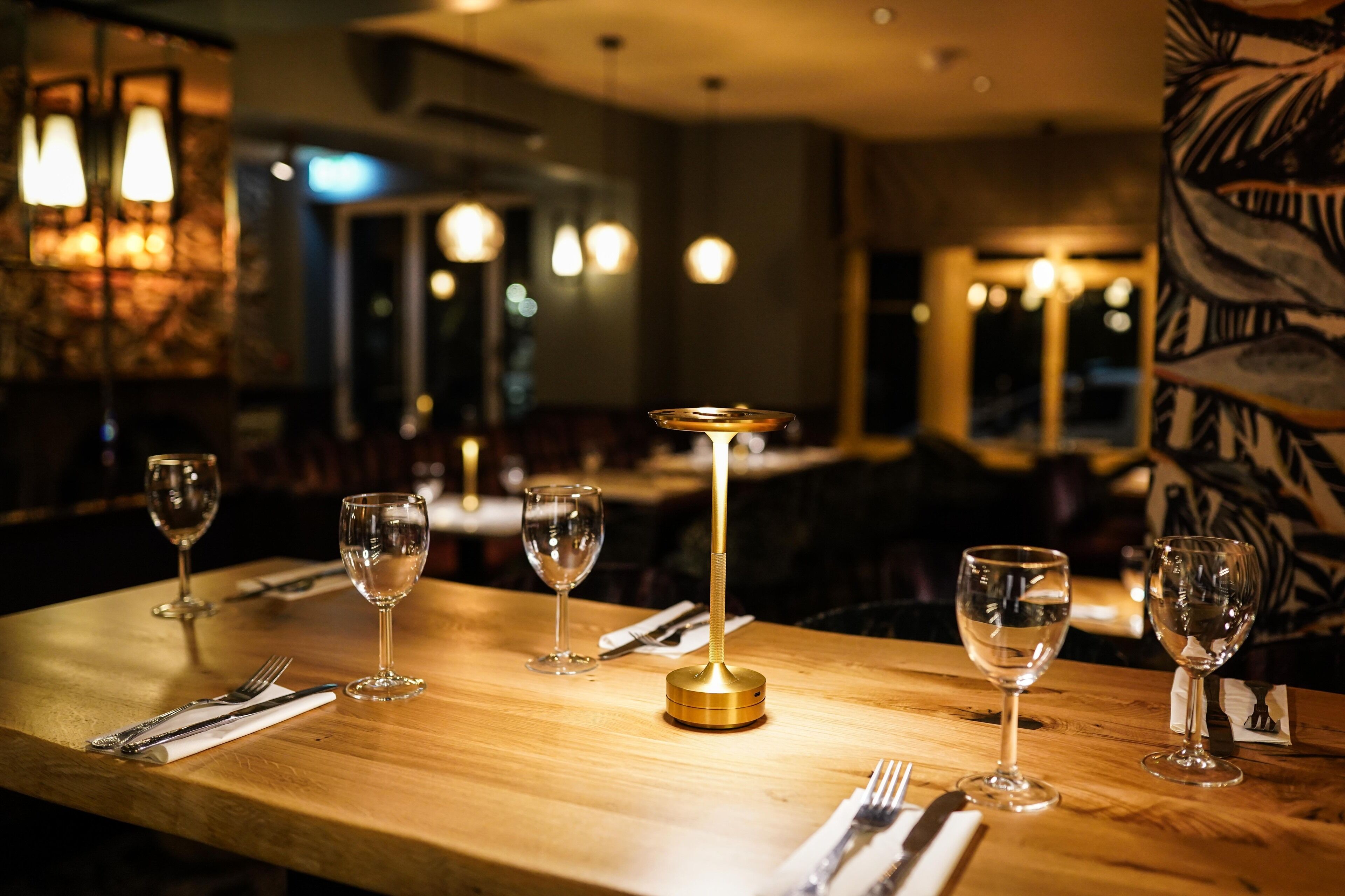 A dining table with a gold base, surrounded by empty wine glasses and cutlery, in a dimly lit restaurant setting.
