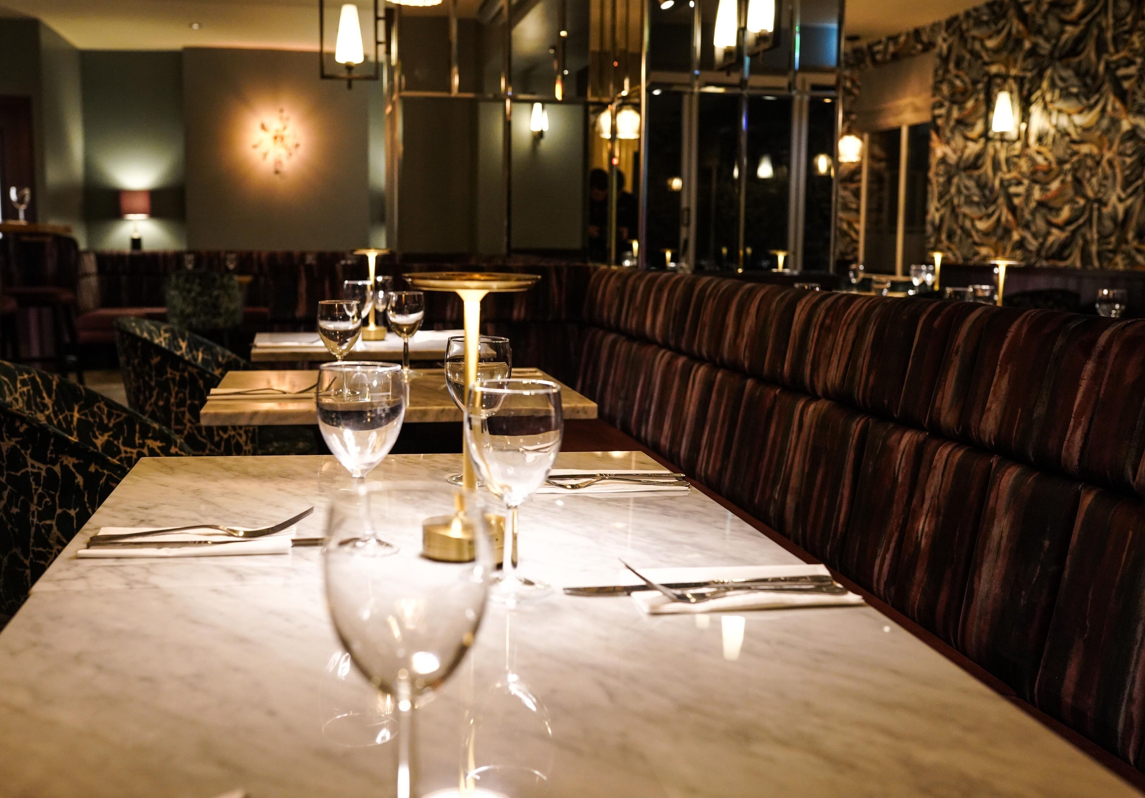 A restaurant with marble tables, wine glasses, and a patterned wall.