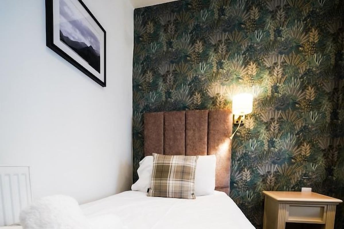 A bed with a plaid blanket, a headboard, a bedside table, and a wall with a framed picture.