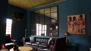 Ein Zimmer mit großem Fenster, einer Ledersofa, einer Lampe und einem Gemälde an der Wand.