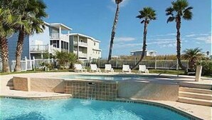 A swimming pool with lounge chairs, palm trees, and a white fence. - Views of Ocean, Boardwalk to Beach and Golf Cart Included, Private Heated Pool, Pet Friendly (Port Aransas)