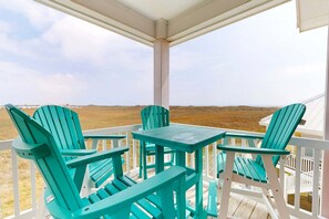 Ein überdachter Außenbereich mit zwei grünen Adirondack-Stühlen und einem kleinen Tisch, mit Blick auf eine karge Landschaft.