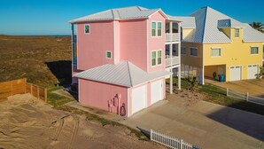 A pink and yellow house with a balcony and a garage. - Views of Ocean, Boardwalk to Beach and Golf Cart Included, Private Heated Pool, Pet Friendly (Port Aransas)