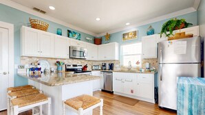 A kitchen with white cabinets, a stainless steel refrigerator, and a central island with stools. - Views of Ocean, Boardwalk to Beach and Golf Cart Included, Private Heated Pool, Pet Friendly (Port Aransas)