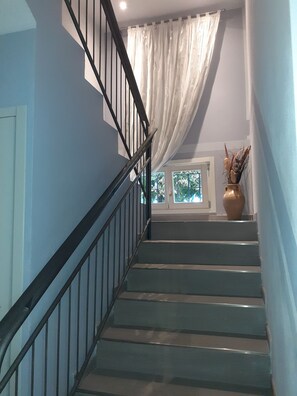 A staircase with black railings leading to a landing with a window and a vase of dried plants. - Royal Room & Breakfast (Modena)