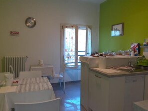 A room with a dining table, chairs, a window with curtains, a radiator, a sink, and a green wall.