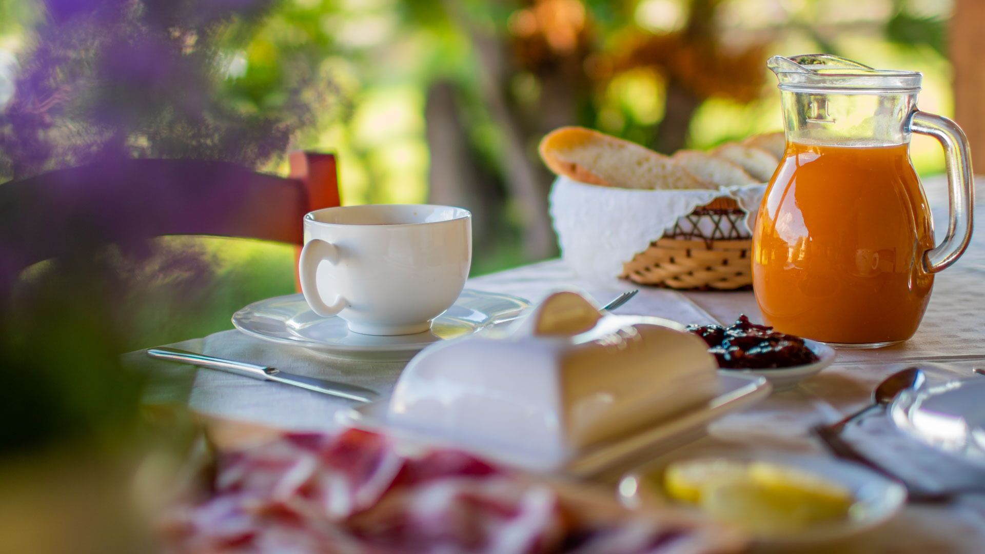 A breakfast setting with a jug of orange juice, a cup, and various food items on a table.