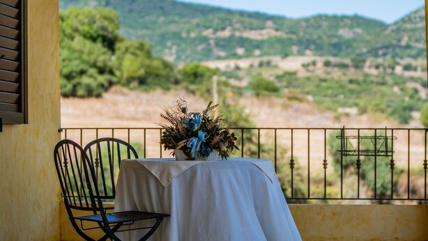 Un balcon avec une table et des chaises, offrant une vue panoramique sur un paysage pittoresque composé de collines et d’arbres.