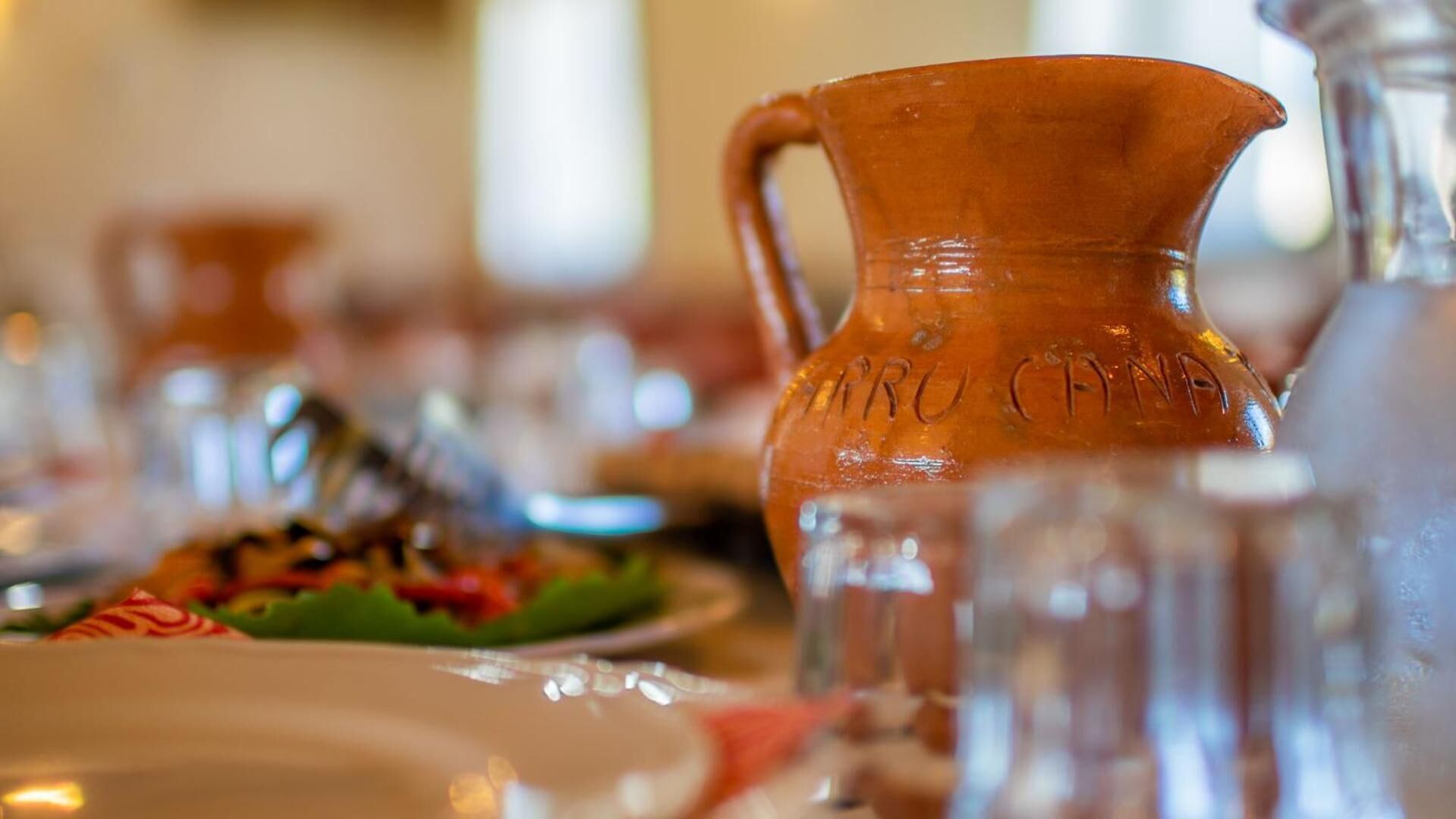 Una mesa con una jarra de cerámica y cristalería, evocando un ambiente para comer.