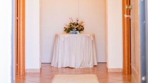Un couloir avec une table blanche placée sous une porte en arc de cercle, une plaque en bois au-dessus, et une petite statue posée sur la table.
