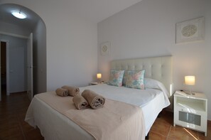 Una cama bien hecha con toallas enrolladas, una lámpara de noche y una mesita de noche con cajón.