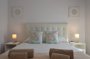 A neatly made bed with floral pillows, two bedside lamps, and two wall-mounted decorative pieces.