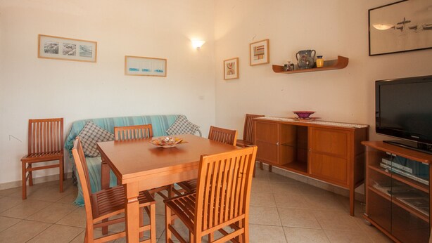 Un área de comedor con una mesa y sillas de madera, un sofá, un televisor y un mueble.