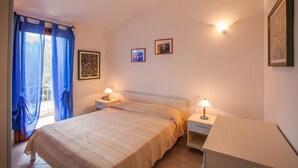 Ein Schlafzimmer mit einem Bett, zwei Nachttischen mit Lampen, einem Fenster mit blauen Vorhängen und zwei gerahmten Bildern an der Wand.