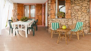 Un patio con muro de piedra, contraventanas de madera, una mesa con sillas y una pequeña mesa redonda con un cuenco.