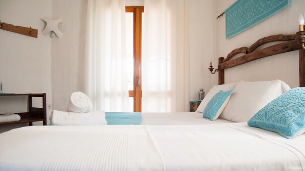 Habitación de hotel con dos camas, cabecero de madera, mesita de noche, lámpara y ventana con cortinas.