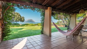 A hammock under a wooden pergola with a view of a grassy area and a distant island.