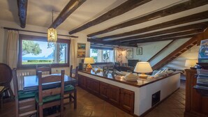 A kitchen with wooden beams, a dining area with a table and chairs, and a view of the sea through large windows.