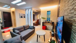 A modern living room with a grey sofa, a round coffee table, and a flat-screen TV mounted on a textured wall. - Overlooking (Antipolo)
