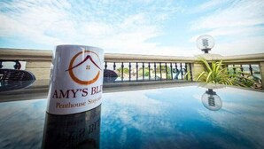 A clear view of a balcony with a railing, a potted plant, and a table with a mug labeled "AMY'S BLD Penhouse Staycation". - Overlooking (Antipolo)