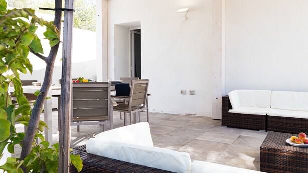 An outdoor patio area with a dining table and chairs, a wicker sofa, and a wicker coffee table with fruit.