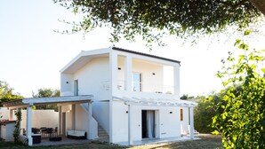 A modern two-story house with a covered patio, outdoor seating, and a staircase leading to the upper floor.