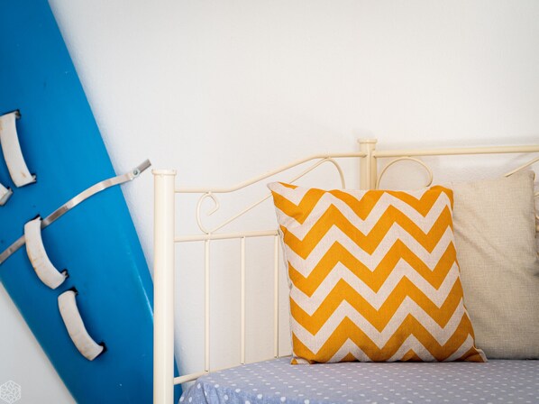 Una cama con estructura metálica blanca, colchón azul y almohada con diseño en zigzag.
