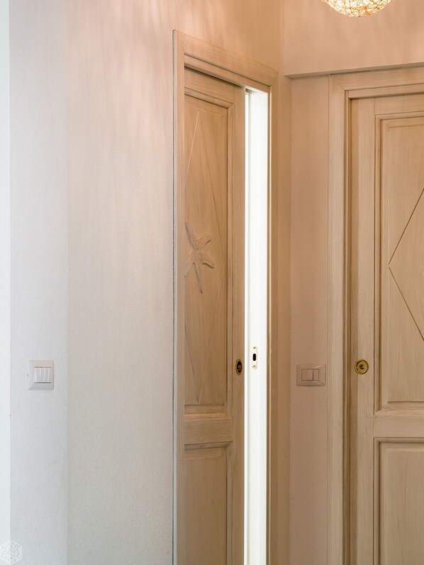 Un pasillo con dos puertas de madera, una abierta que da a una escalera, e interruptores de luz en la pared.