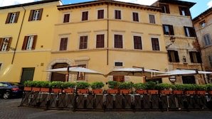 A yellow building with multiple windows and a balcony. There are potted plants in front of the building. - Margana Palace by ROMAC (Rome)
