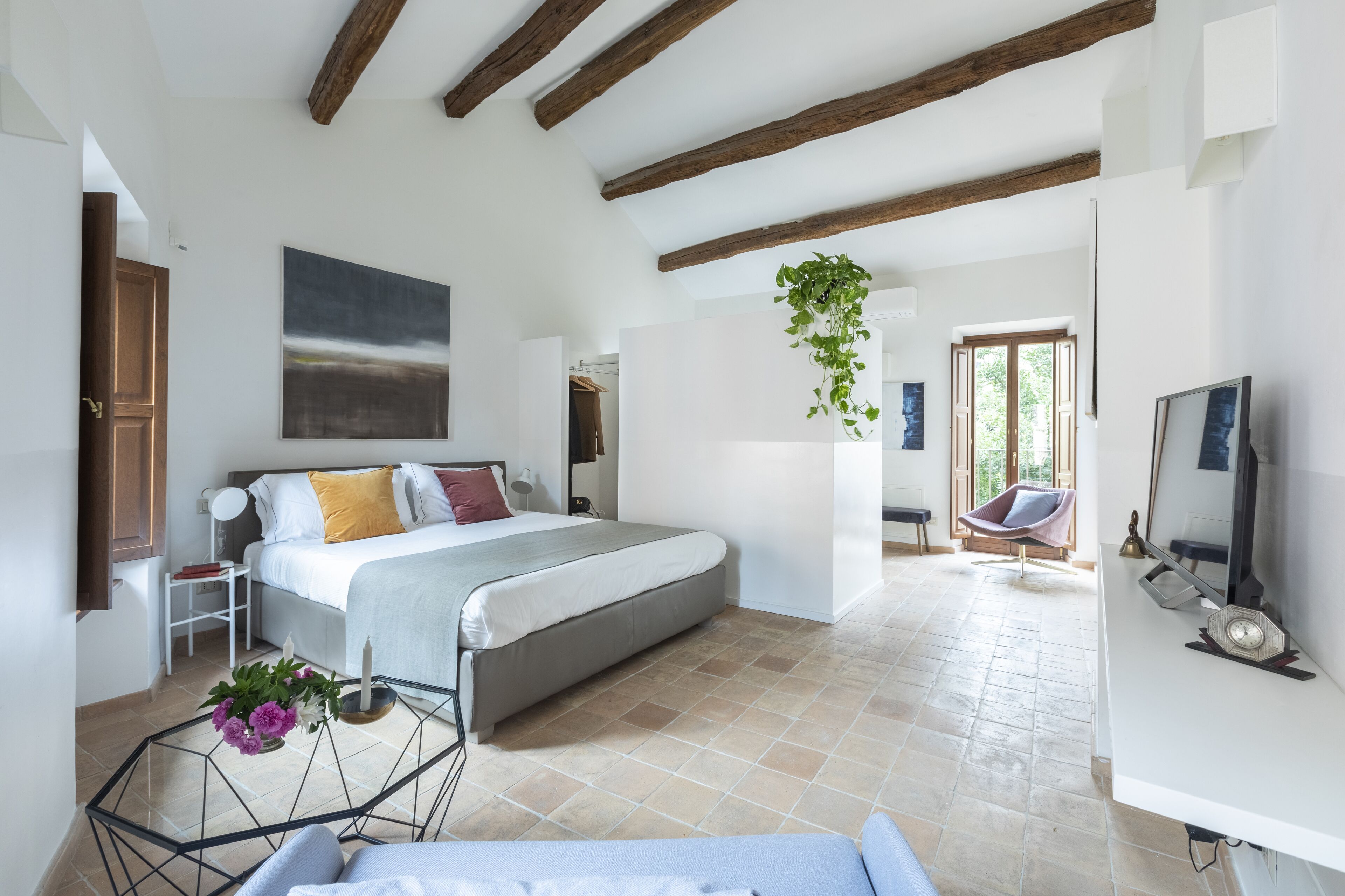 A bedroom with a bed, bedside table, and a hanging plant.