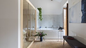 A modern bathroom with a glass shower enclosure, a white bathtub, and a bench. - Margana Palace by ROMAC (Rome)