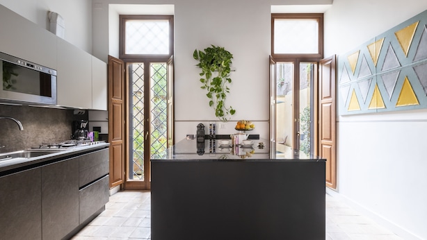 A modern kitchen with a central island, built-in appliances, and a view through glass doors. - Margana Palace by ROMAC (Rome)