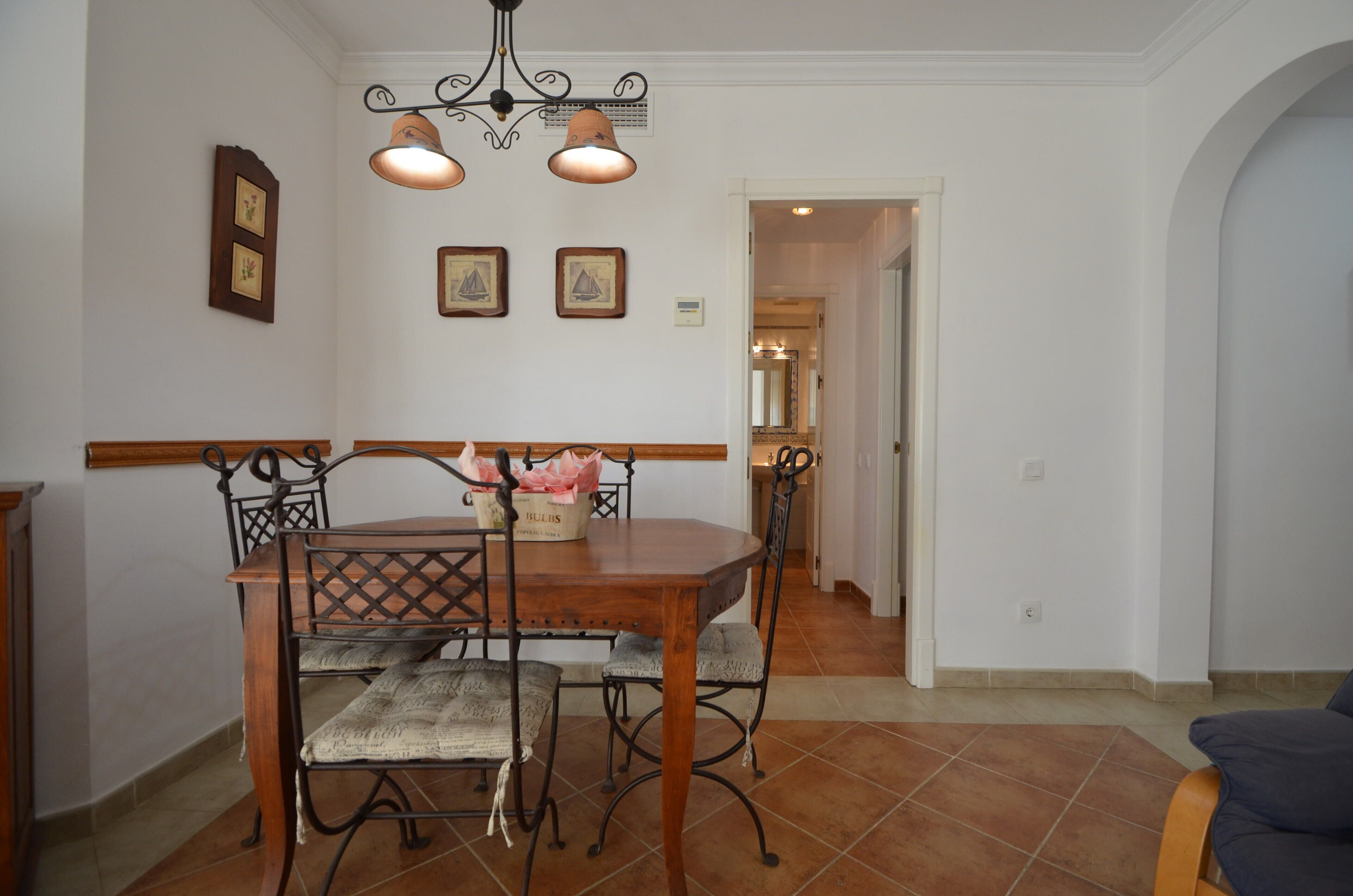 A dining area with a wooden table and chairs, a chandelier, and framed pictures on the wall.