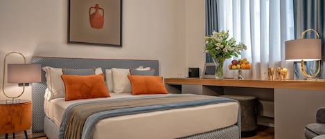 A modern hotel room with a bed, a desk, and a chair. There is a painting on the wall and a vase with flowers on the desk.