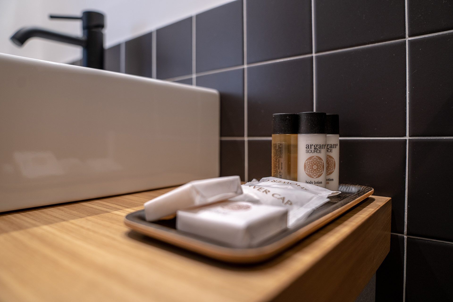 Uma bancada de banheiro com uma pia branca, um porta-objetos com amenities e uma embalagem de loção corporal.